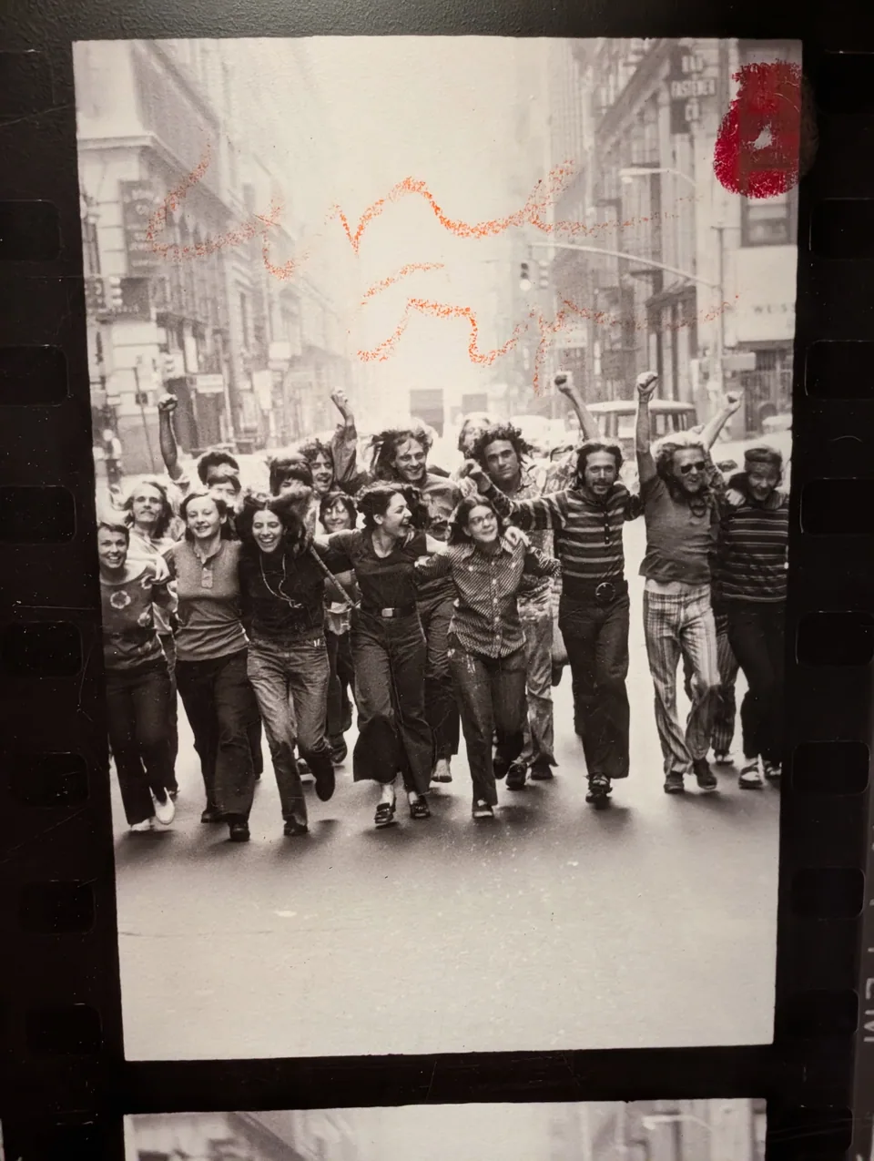 A displayed black-and-white photograph of people marching, marked with red handwriting.