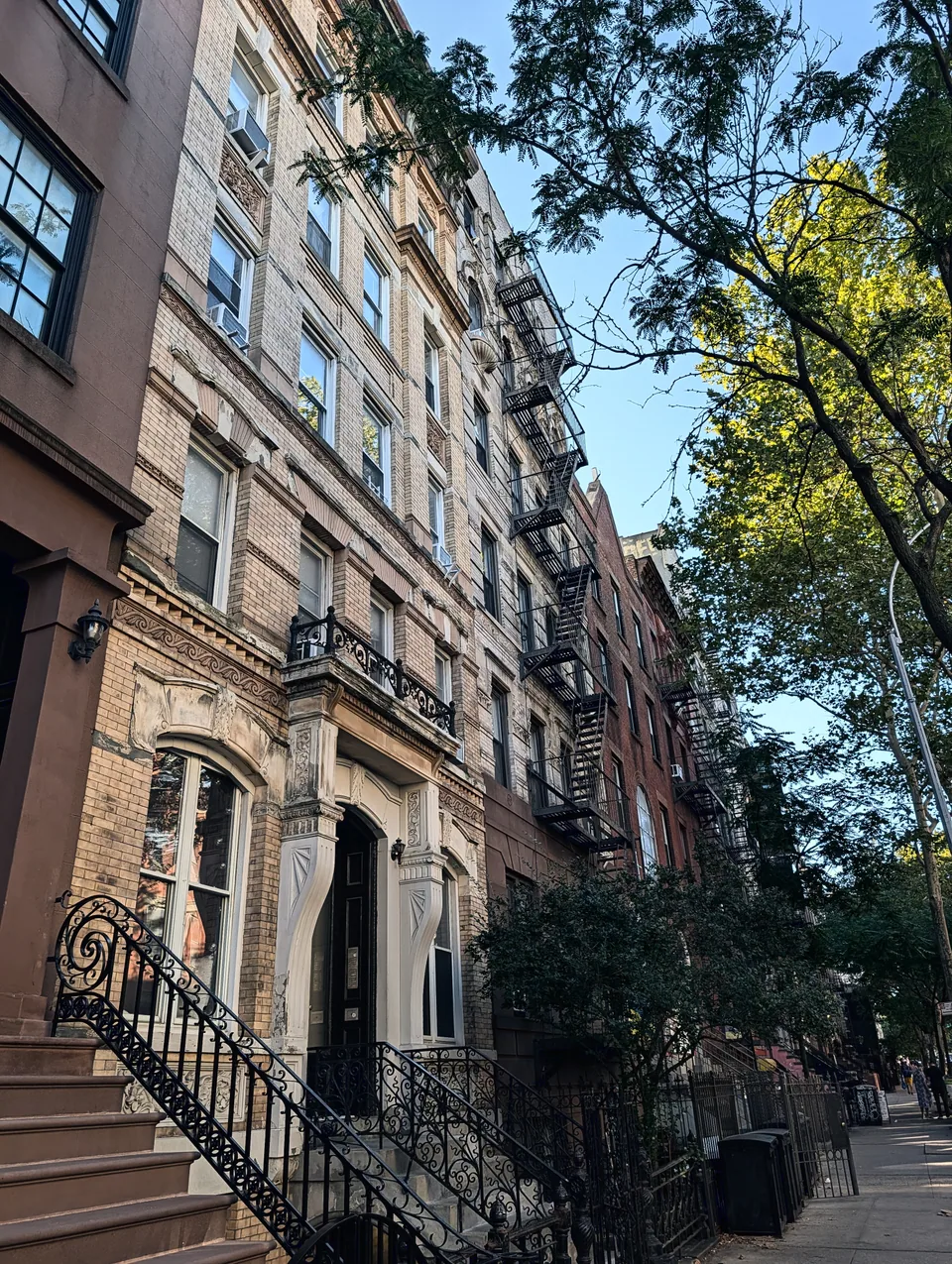 Brownstone buildings and iron staircases beneath leafy trees in New York.