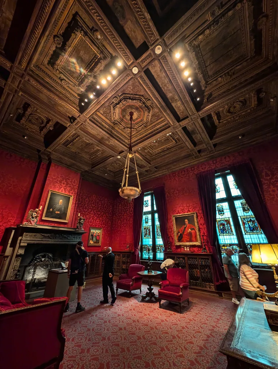 An ornate wood ceiling above a red room and visitors at the Morgan Library.