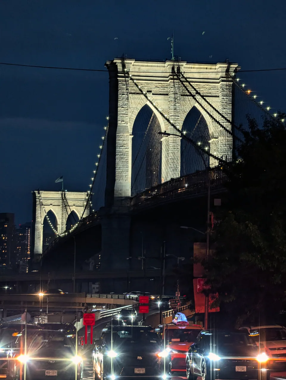 The illuminated Brooklyn Bridge above traffic and headlights at blue hour.