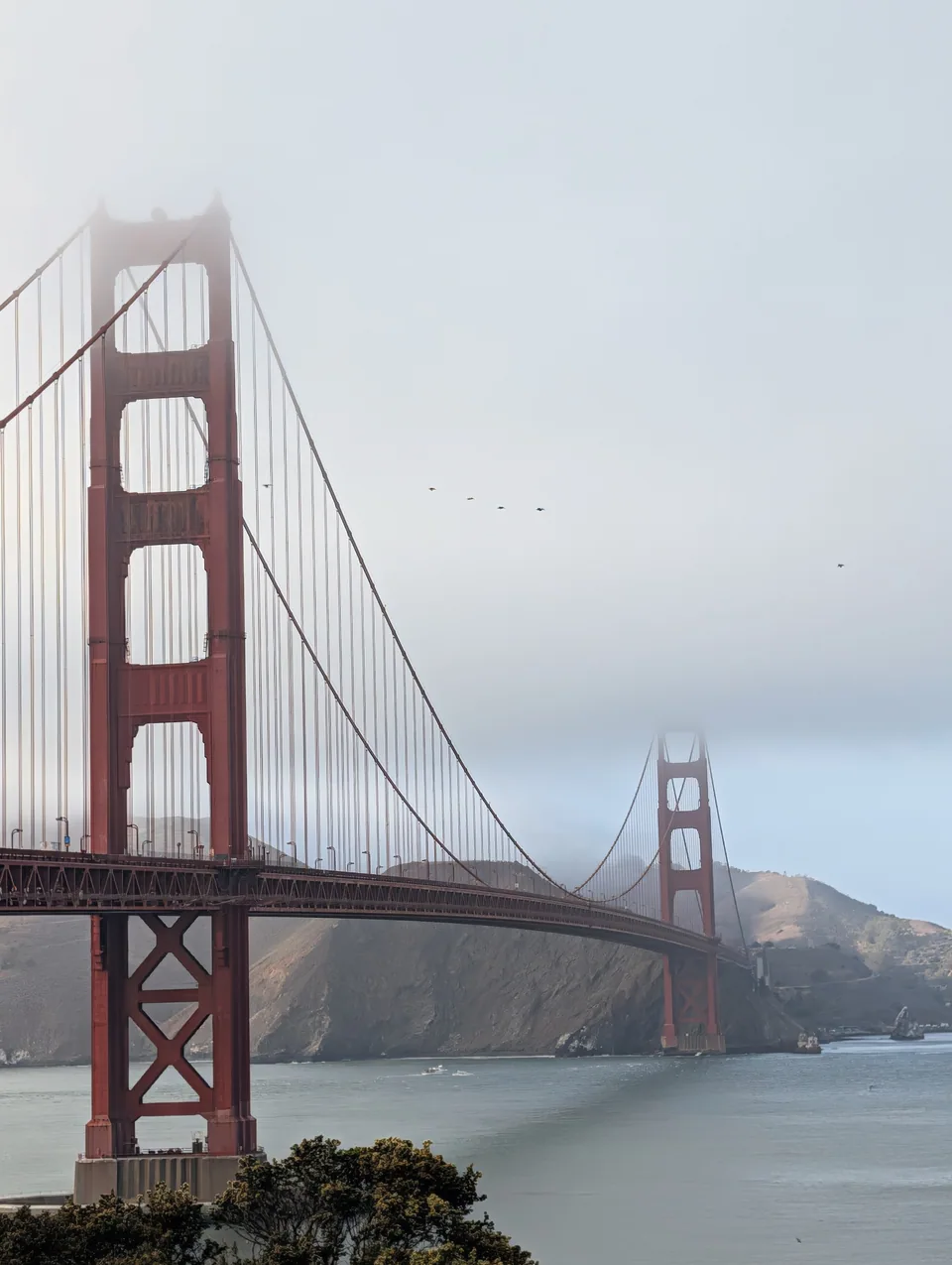 The Golden Gate Bridge disappearing into fog over grey water.