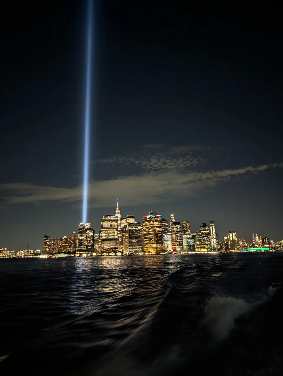 The Manhattan skyline at night across dark water, with two blue beams of light.