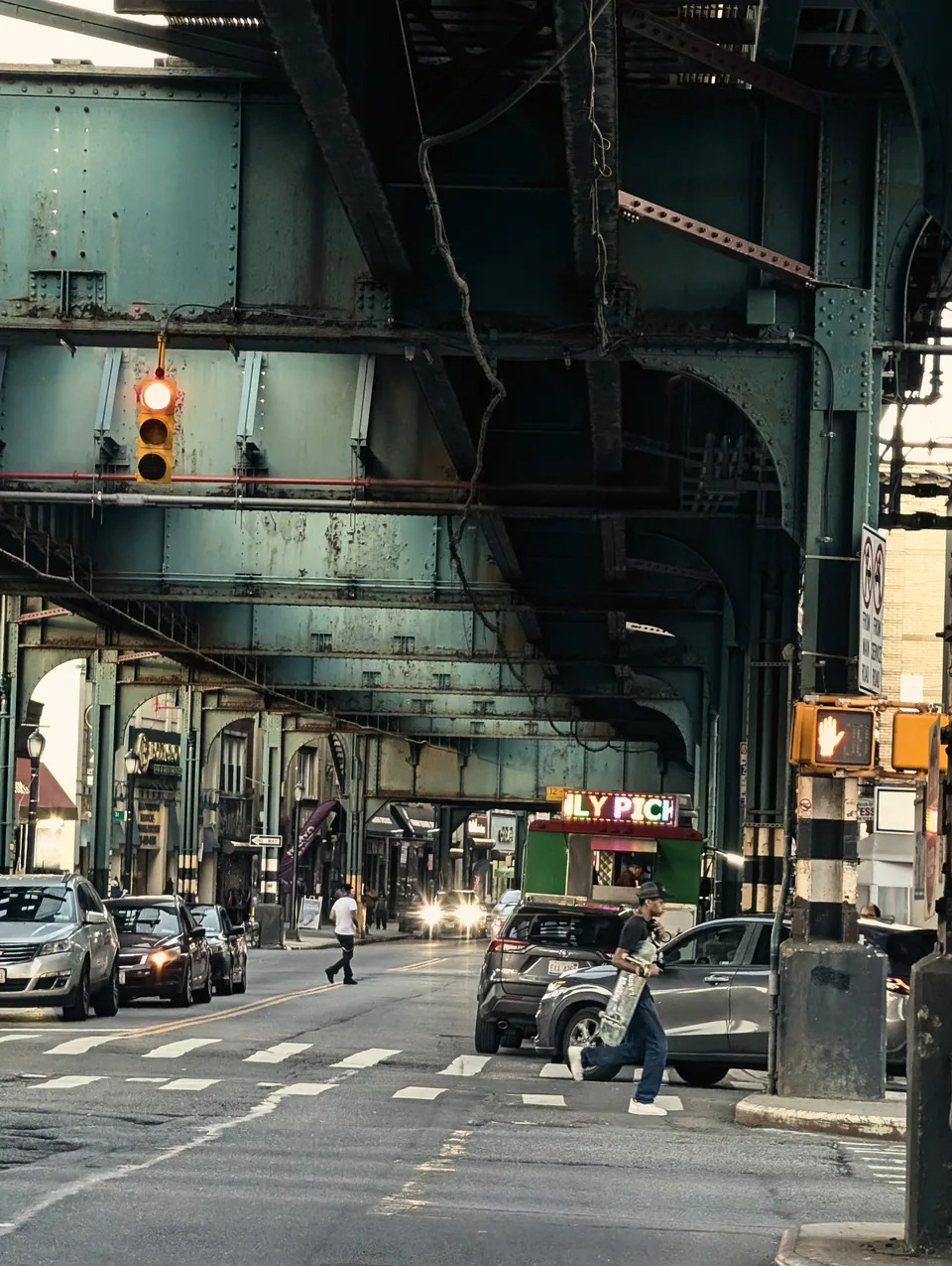 A street and traffic light beneath green elevated railway girders in New York.