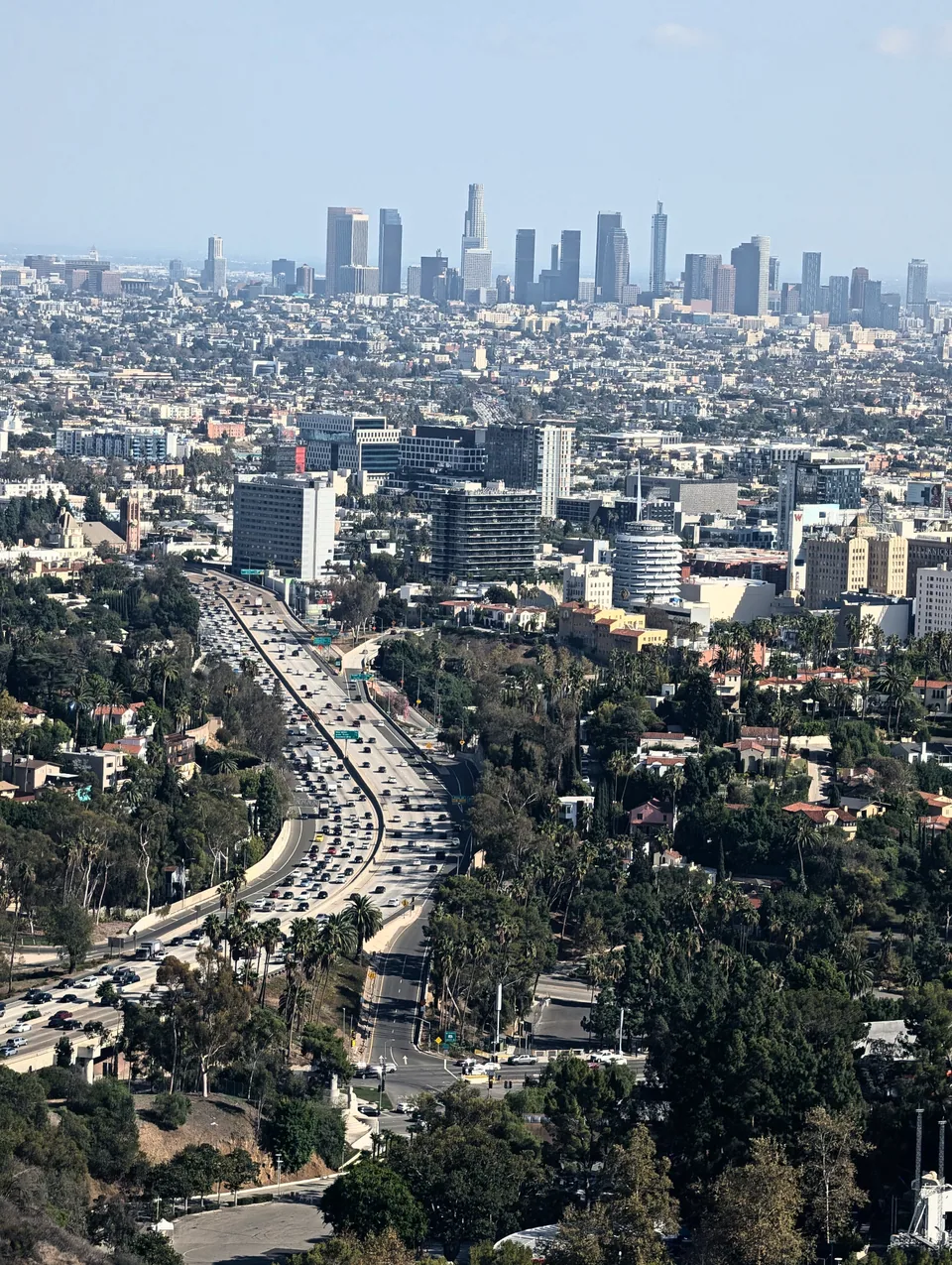 A curving highway leading towards the Los Angeles skyline in the daylight haze.